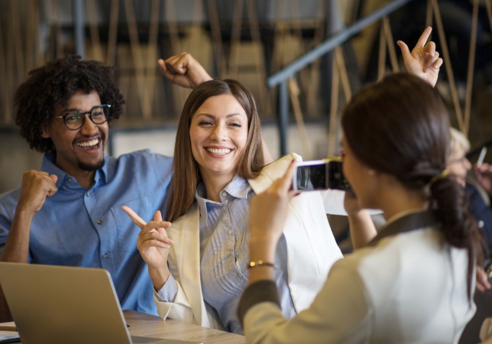 Das Bild zeigt mehrere junge Menschen in einem Büro, die hinter einem Laptop sitzen und glücklich aussehen, da sie sich über Corporate Benefits freuen.