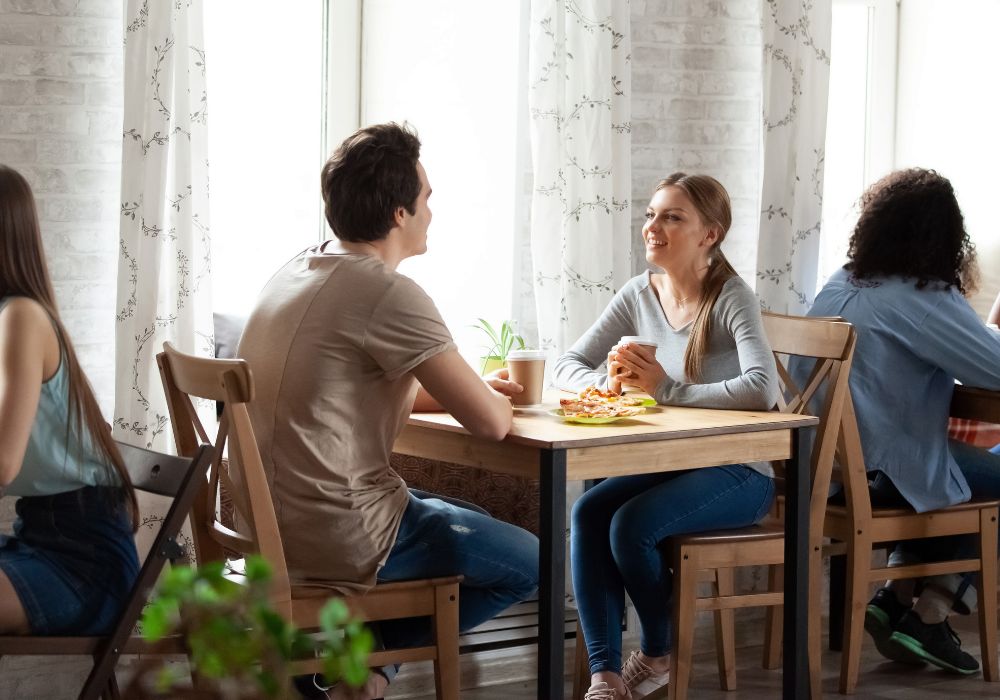 Sur l'image il y a deux personnes assises à une table d'un café ou restaurant. Ils sont en train de parler et peut-être en améliorer leur allemand.